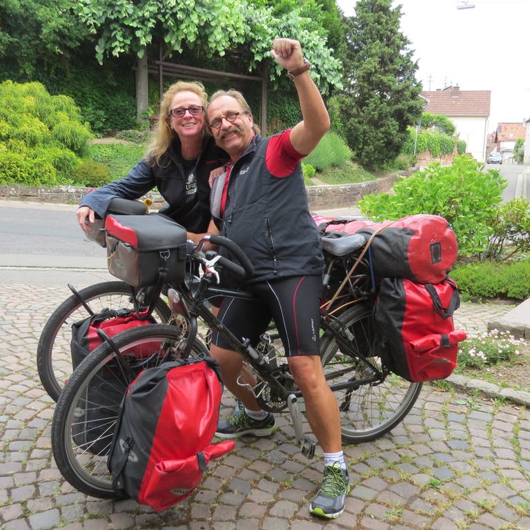 Eine Frau und ein Mann in Fahrradkleidung mit ihren bepackten Fahrrädern.