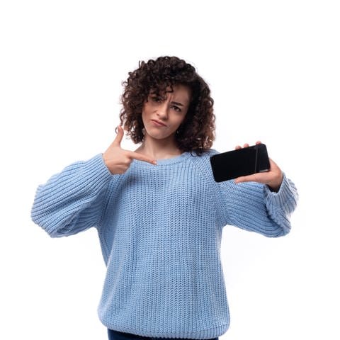 Eine junge Dame mit schwarzen Locken und einem hellblauen Pullover zeigt den Bildschirm auf einem Handy.